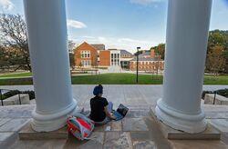 Female student sitting on the steps between the columns of H.J. Patterson, view looking torwards Edward. St John Learning and Teaching Center.