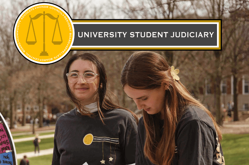 Picture of 2 students within USJ at a tabling event with the USJ logo added on to the image. Logo for USJ: Yellow circle with branches around a scale. 